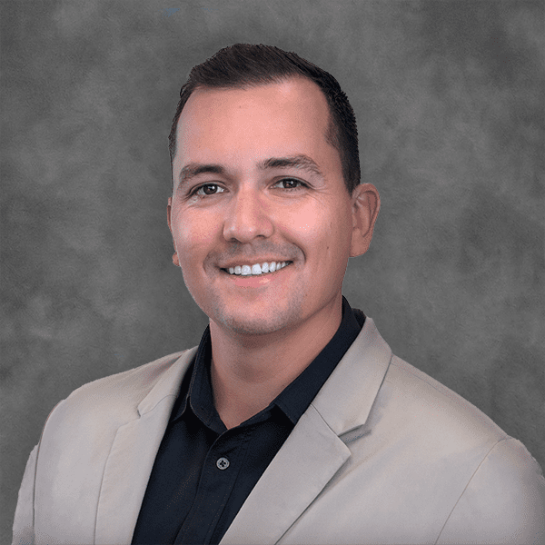 Smiling man in blazer against gray background.